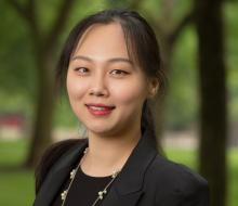 Headshot of Anna Zhao smiling at the camera. She is wearing a black blazer, long gold necklace, and her hair in a ponytail with long side bangs.