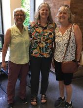 Three casually dressed women standing with their arms around each other and smiling for the camera