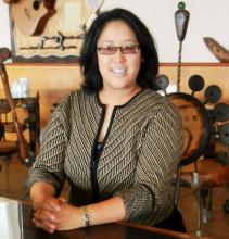 An upper-body shot of Professor Regina Lee, an asian woman wearing glasses with shoulder-length, dark brown hair, and wearing a button up cardigan with her hands folded on the table in front of her.