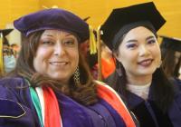 Upper body shot of two women wearing graduation gowns and caps and smiling at the camera