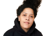 Upper body shot of a Black woman wearing a black hoodie and her afro in a ponytail. She's looking directly at the camera and has a neutral expression.