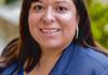 Headshot of Dr. Elizabeth Ramirez Arreola wearing a blue suit jacket over blue lace top. Sporting shoulder length straight brown hair with side swept bangs and a big smile. 