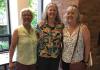 Three casually dressed women standing with their arms around each other and smiling for the camera