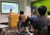 Marielle Marcaida presenting her project to a classroom of students. She is standing behind a lectern and on the screen behind her it reads: "Marielle Y. Marcaida, Department of Gender, Women & Sexuality Studies, PhD in Feminist Studies."