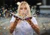 Woman with blonde hair and wearing a plain white t-shirt is holding an open book with multi-colored confetti exploding out of it.