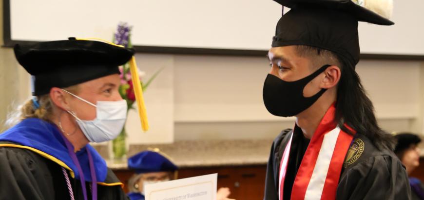 Side shot of Hadi Yusri accepting certificate for minor in GWSS from Professor Amanda Swarr. Both are wearing full graduation regalia.