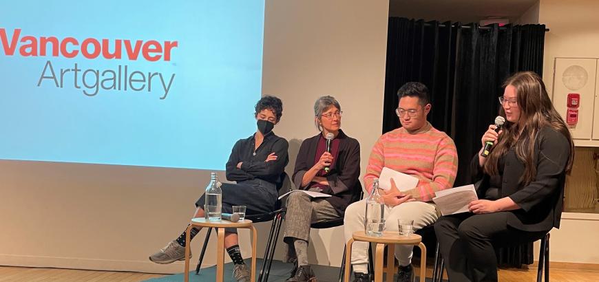 Sasha Welland sitting on a small stage with three panelists