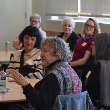 A seated group of Fall Reception attendees listening as one woman speaks.