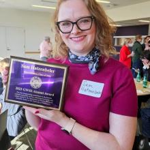 Headshot of a woman holding up an award plaque.